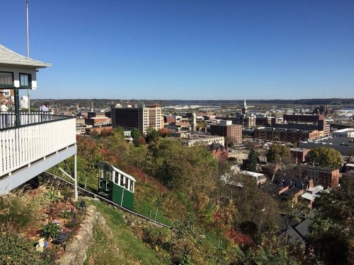 A scenic view of a city from a hilltop, featuring a funicular railway and clear blue skies.