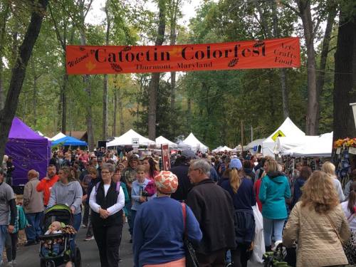 Crowd at Catoctin Colorfest in Thurmont, Maryland, with colorful tents and a festive banner overhead.