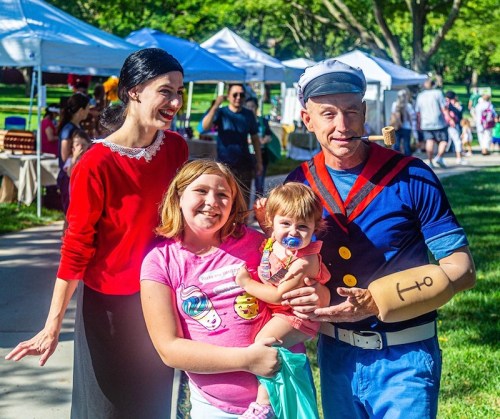 A family poses with a man dressed as Popeye and a woman in a red top, smiling at a community event.