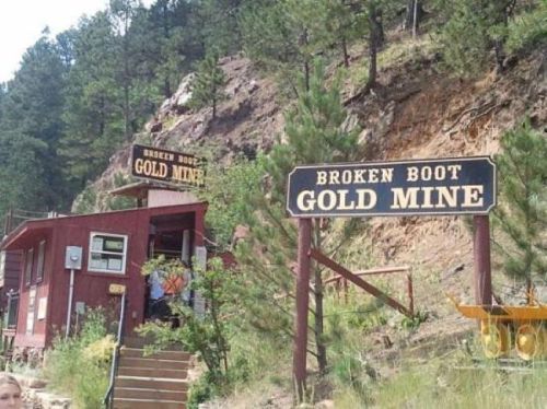 Signage for "Broken Boot Gold Mine" with a rustic building and trees in a mountainous area.