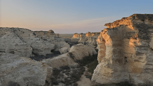 A scenic view of rugged, white rock formations and canyons under a soft sunset sky.