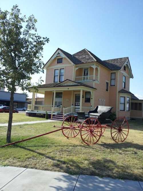 A large yellow Victorian house with a horse-drawn carriage in front, surrounded by grass and trees.