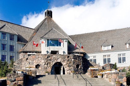Historic stone building with a triangular roof, featuring flags of Canada, Japan, the USA, and the UK at the entrance.