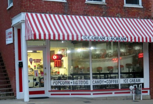 A quaint ice cream shop with a red and white striped awning, featuring a menu of snacks and a welcoming "OPEN" sign.