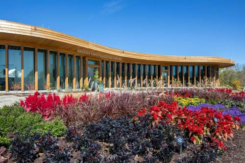 Modern building with a curved wooden facade, surrounded by vibrant flower beds under a clear blue sky.