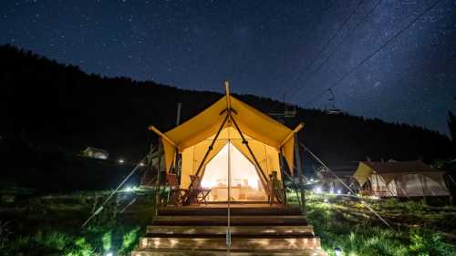 A cozy glamping tent illuminated at night, surrounded by grass and under a starry sky.