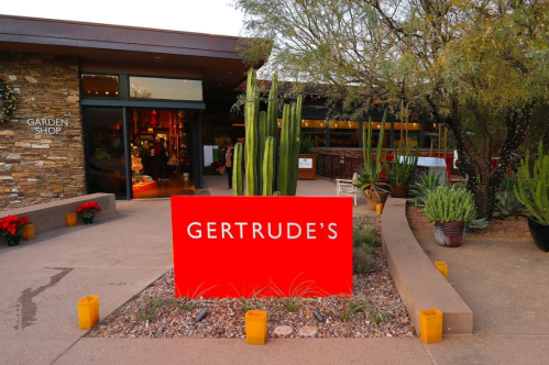Exterior view of Gertrude's restaurant with a red sign, surrounded by desert plants and a garden shop entrance.
