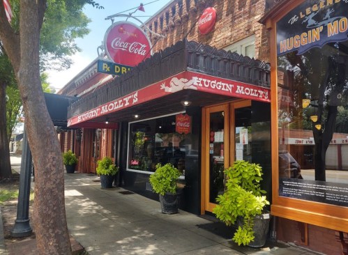 Exterior of Huggin' Molly's restaurant with a Coca-Cola sign, featuring potted plants and a welcoming entrance.