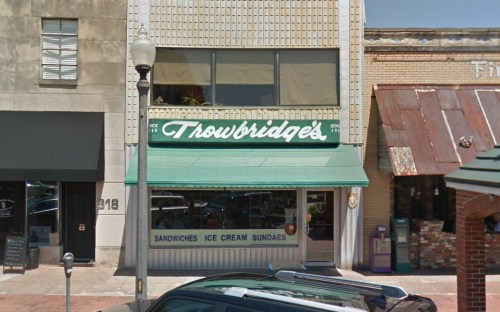 A storefront with a green awning reading "Throwbridge's" and signs for sandwiches and ice cream sundaes.