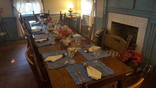 A dining table set for a meal, featuring blue checkered placemats, glassware, and floral centerpieces.