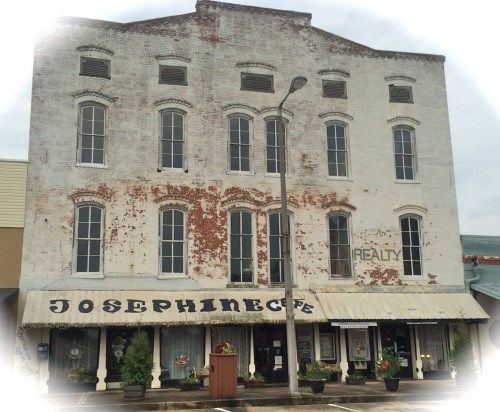 Historic brick building with large windows, featuring a "Josephine Cafe" sign and a "Realty" sign above.