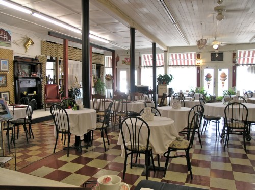 A cozy, vintage-style restaurant with round tables, checkered floors, and decorative elements like plants and wall art.