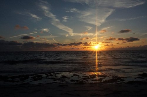 Sunset over the ocean, with vibrant colors reflecting on the water and wispy clouds in the sky.