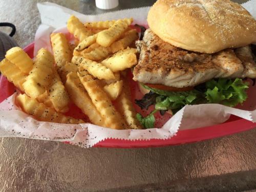 A grilled fish sandwich with lettuce and tomato, served with a side of crinkle-cut fries on a red tray.