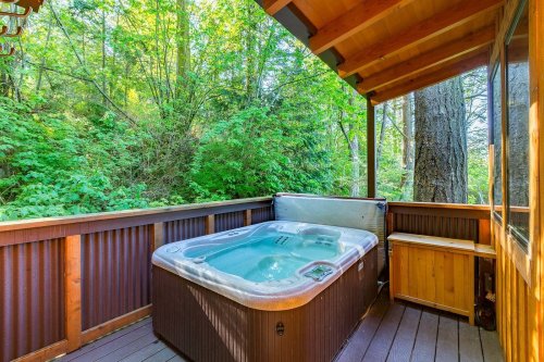 A hot tub on a wooden deck surrounded by lush green trees and foliage.