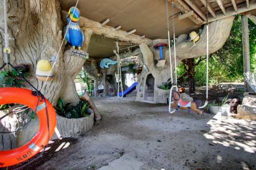 A whimsical play area with swings, slides, and tree-like structures, surrounded by greenery and playful decorations.