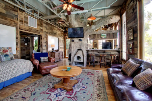 Cozy living room with rustic wood decor, a large tree feature, leather furniture, and a round coffee table.