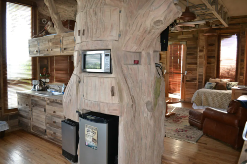 Cozy interior of a rustic cabin featuring a tree trunk kitchen island, wooden decor, and a warm living space.
