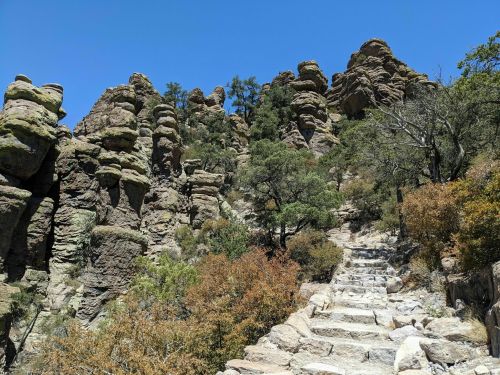 Rocky landscape with steep stone steps leading up through trees and shrubs under a clear blue sky.
