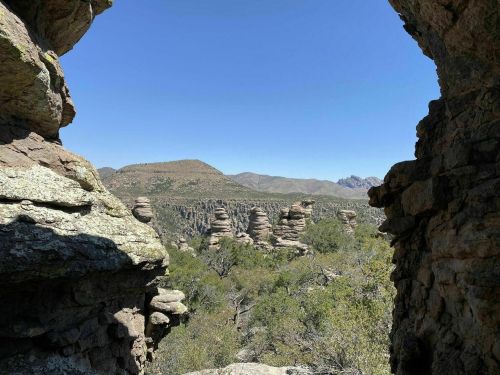 A scenic view of rocky formations and mountains under a clear blue sky, framed by stone walls.