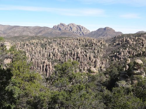 A panoramic view of unique rock formations and mountains under a clear blue sky, surrounded by greenery.
