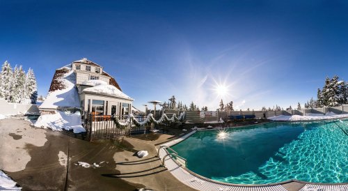 A snowy landscape featuring a pool and a building, with clear blue skies and the sun shining brightly.