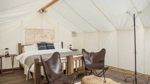 Cozy tent interior with a large bed, two chairs, and rustic decor, creating a comfortable glamping atmosphere.