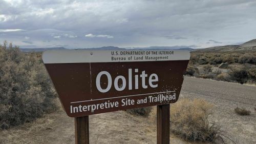 Sign for Oolite Interpretive Site and Trailhead, with a cloudy sky and desert landscape in the background.