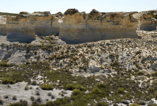 A rocky cliff with layered formations, surrounded by sparse vegetation and a clear blue sky.