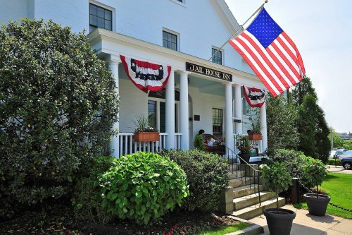 Exterior of Jail House Inn with American flag and decorative bunting, surrounded by greenery and a welcoming entrance.