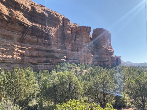Rocky cliffs rise above a green landscape under a clear blue sky, with sunlight illuminating the scene.
