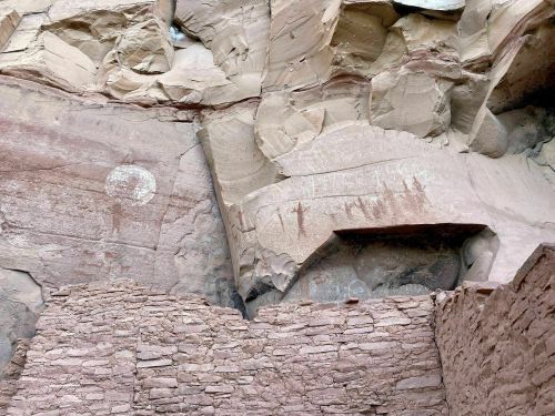 Ancient rock art and petroglyphs on a cliff face, with a stone structure at the base.