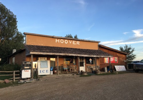 A rustic store named "Hoover" with signs for ice, set against a clear blue sky and surrounded by trees.