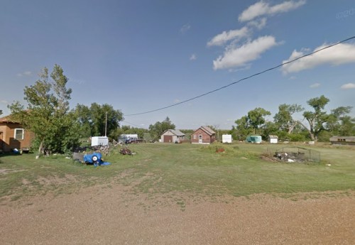 A rural landscape featuring several houses, trees, and open grassy areas under a clear blue sky.