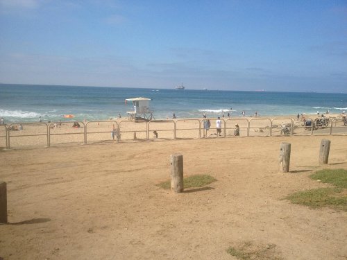 A sandy beach with a lifeguard tower, people enjoying the sun, and gentle waves under a clear blue sky.