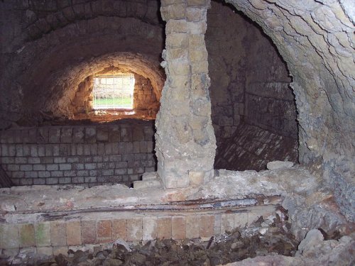 Interior of a stone structure with an arched ceiling, featuring a window and debris on the floor.