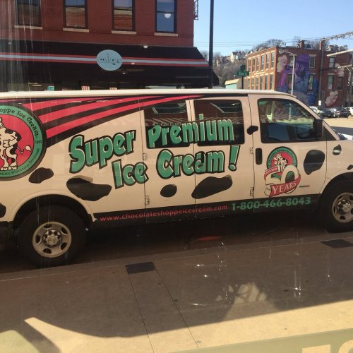 A colorful ice cream van with a cow print design, advertising "Super Premium Ice Cream!" and a contact number.