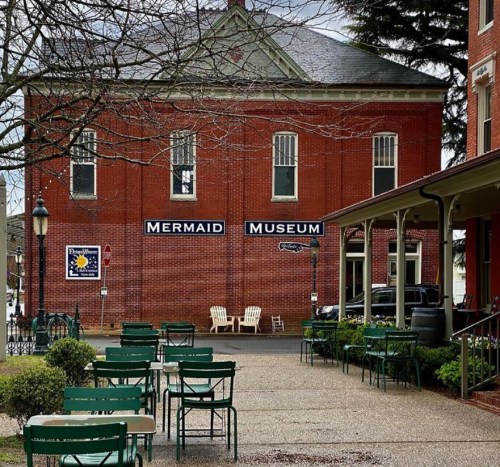 Exterior of the Mermaid Museum, featuring a red brick building and outdoor seating area with green chairs.