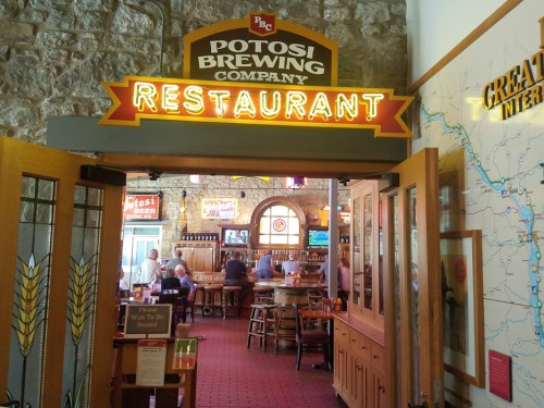 Entrance to Potosi Brewing Company restaurant, featuring a stone wall and a lively dining area in the background.
