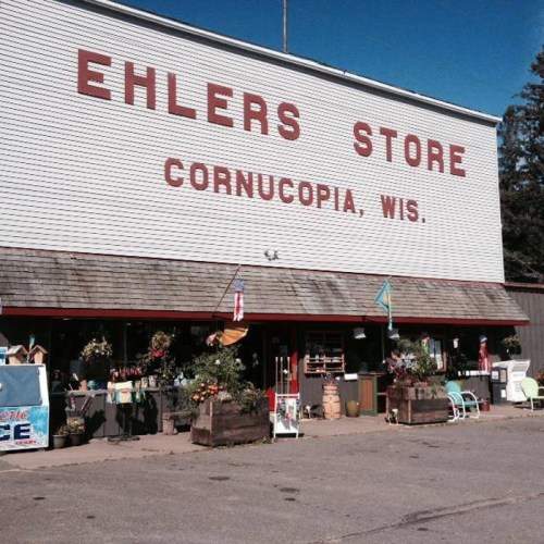 Exterior of Ehlers Store in Cornucopia, Wisconsin, featuring colorful flowers and outdoor seating.