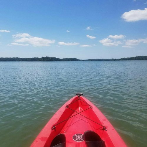 A red kayak on calm water, with a clear blue sky and distant hills in the background.