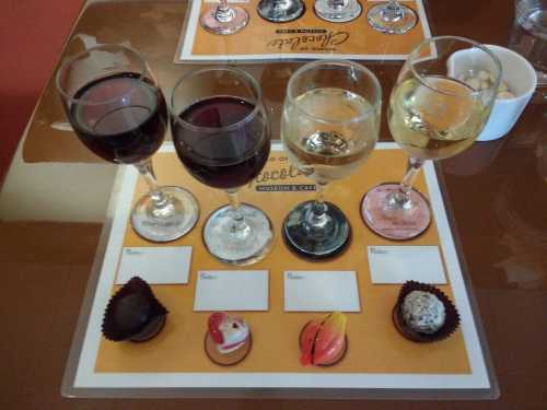 Four glasses of wine (two red, two white) beside a selection of chocolates on a tasting placemat.