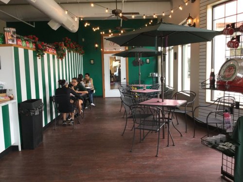 A cozy café interior with green and white striped walls, tables, and chairs, featuring patrons enjoying their time.