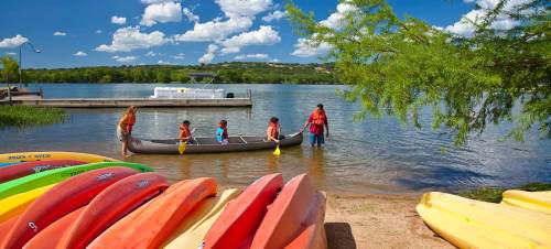 A family enjoys a sunny day by the lake, preparing to kayak while colorful kayaks line the shore.