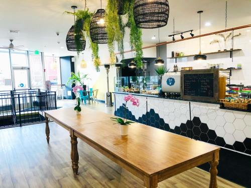 A modern café interior featuring a large wooden table, hanging plants, and a colorful counter with a menu board.
