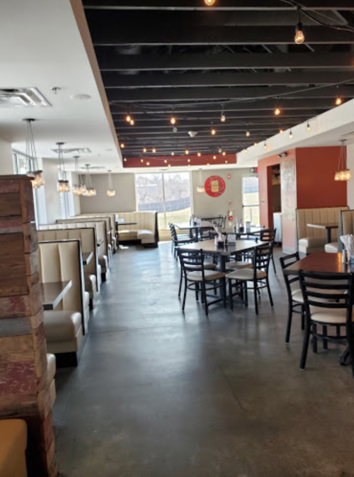 Interior of a modern restaurant featuring booths, tables, and pendant lighting, with a spacious and inviting atmosphere.