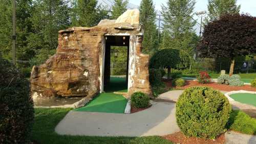 A mini-golf course featuring a rock formation entrance surrounded by neatly trimmed bushes and green turf.