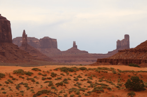 A desert landscape featuring towering rock formations and mesas under a cloudy sky.