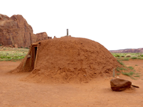 A traditional earthen dwelling with a rounded shape, set against a rocky landscape and grassy ground.