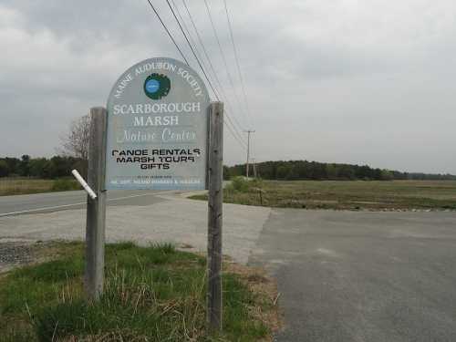 Sign for Scarborough Marsh Nature Center, featuring canoe rentals and tours, near a road and marshland.